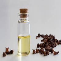 A transparent bottle of clove essential oil with dried cloves on a white background